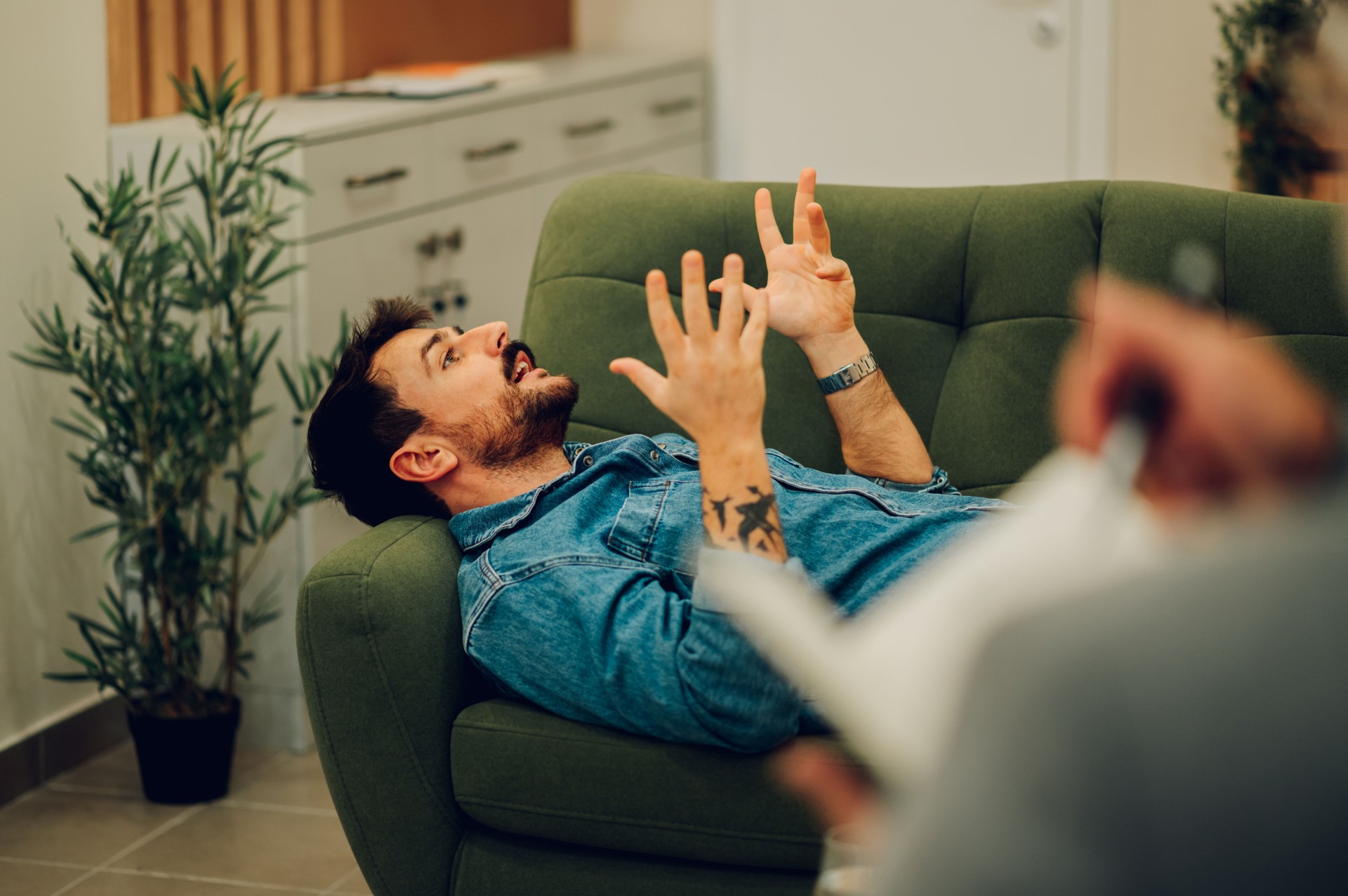 A man with problems is lying down on a sofa in a psychotherapist's office
