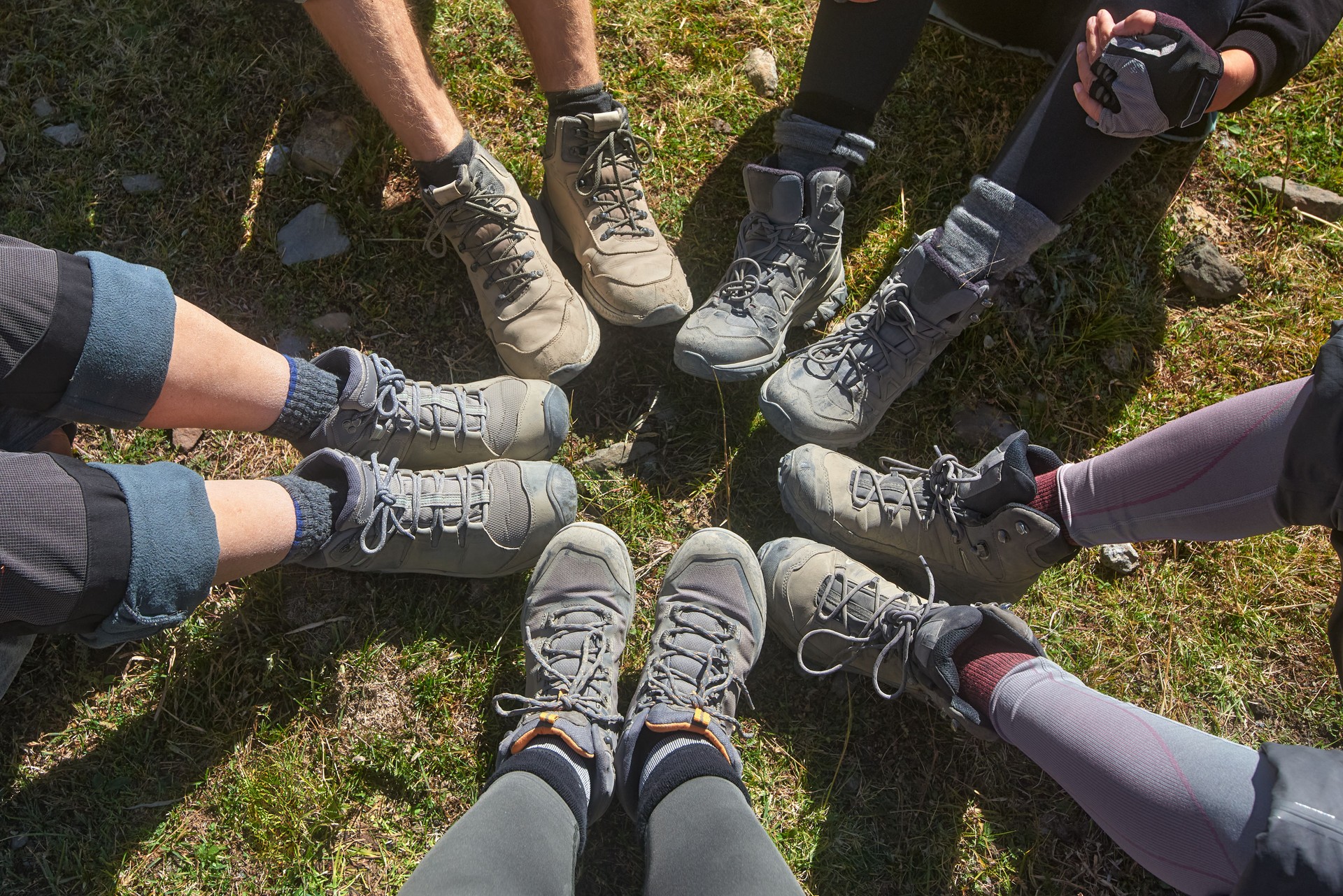 Group of hikers sitting in circle with dusty trekking boots in center and chat during vacation.