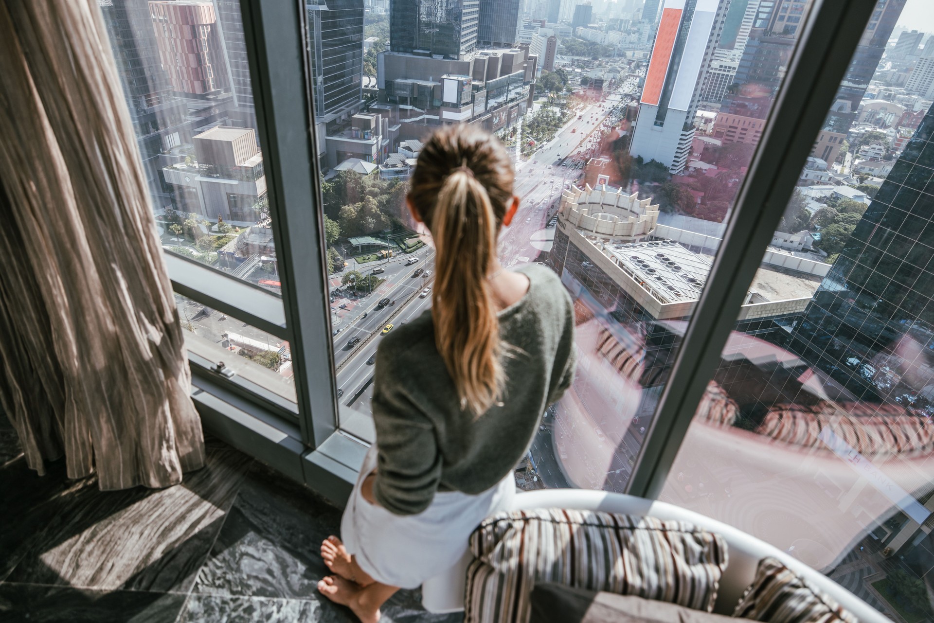 Woman admiring a cityscape from a high-rise apartment.