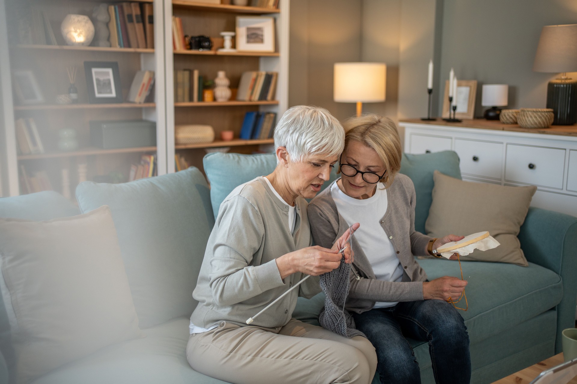 Two senior women knitting and embroidering together at home