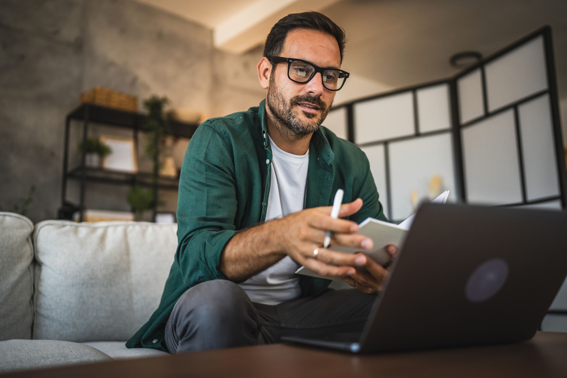 Adult man in green shirt work from home and use laptop and notepad