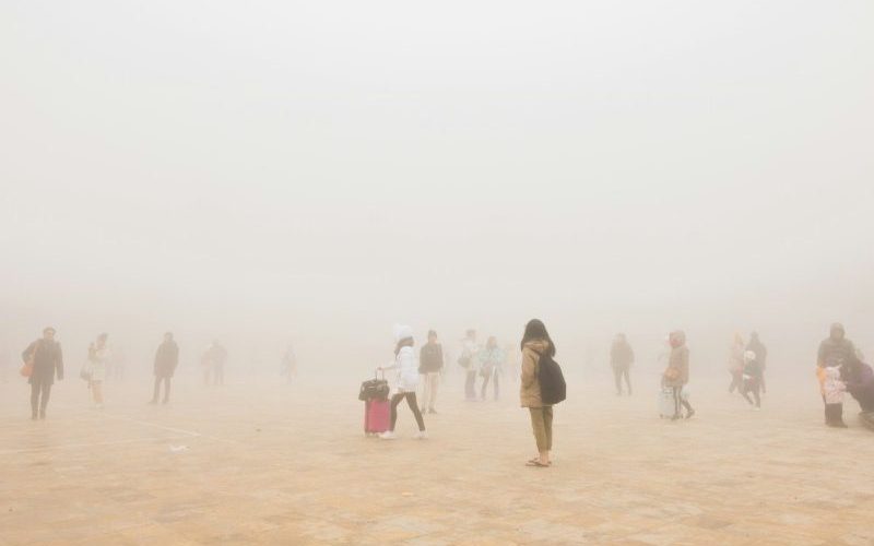 People walking across an open landscape in thick haze.